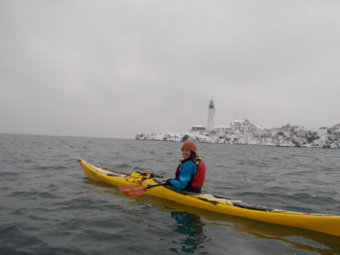 a woman kayaking in winter, bundled up in safety gear